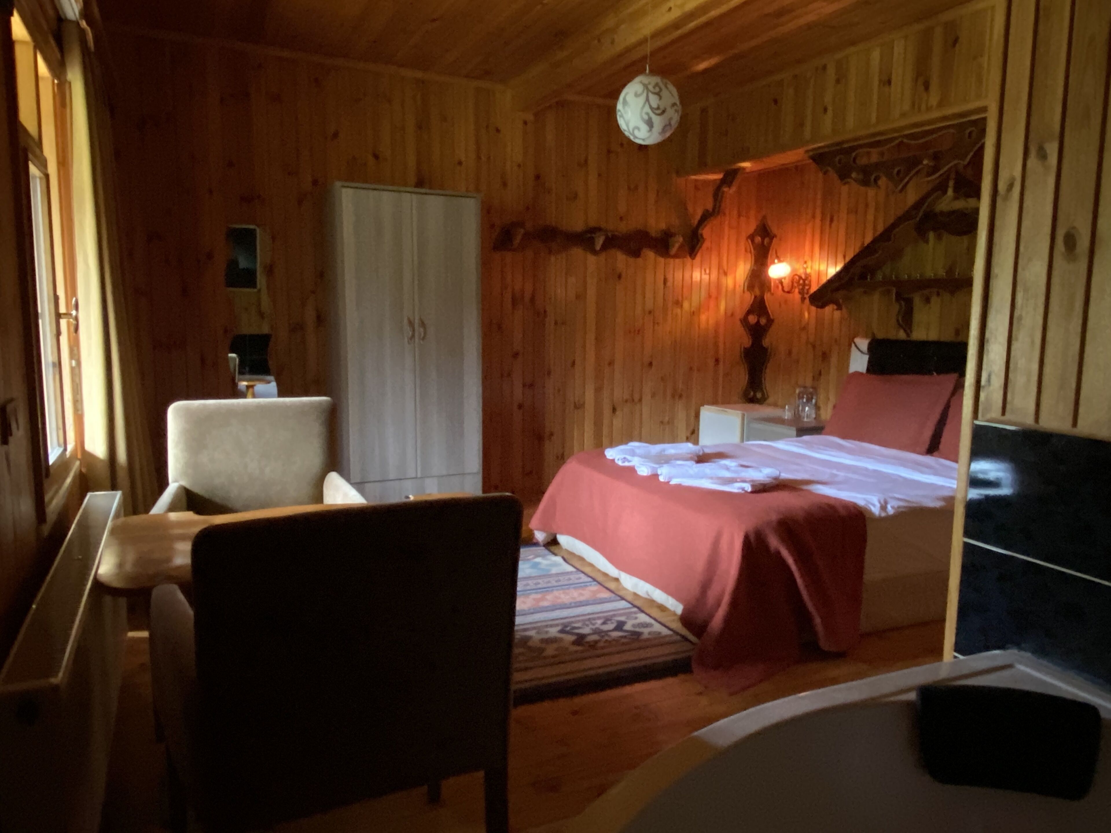 Una habitación de madera con una cama, una silla, un armario y una mesita.