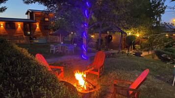 Eine Holzhütte mit Feuerstelle und roten Adirondack-Stühlen im Garten.
