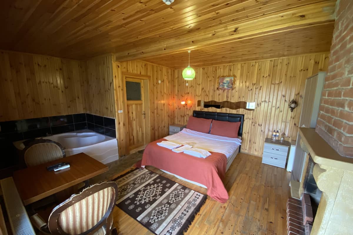 A wooden room with a bed, a desk, a chair, a small table, a rug, and a fireplace.