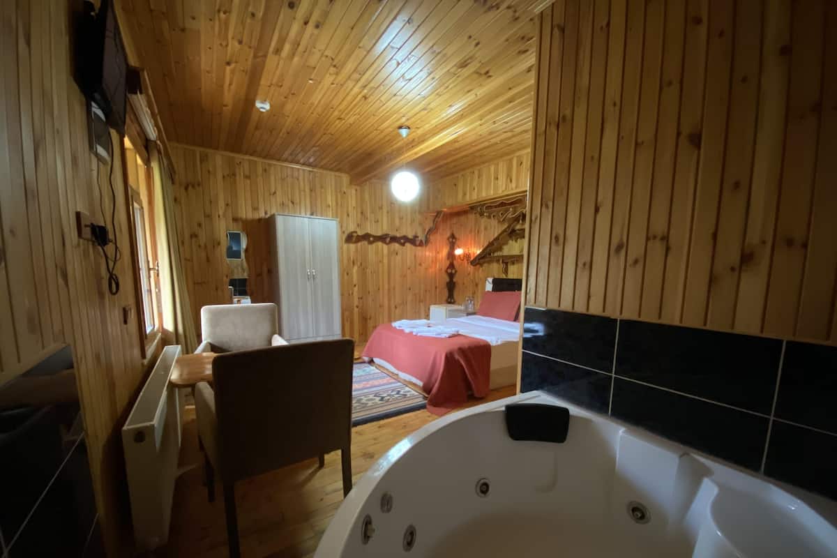 A wooden cabin interior with a bedroom, a bathroom with a bathtub, and a wooden chair.