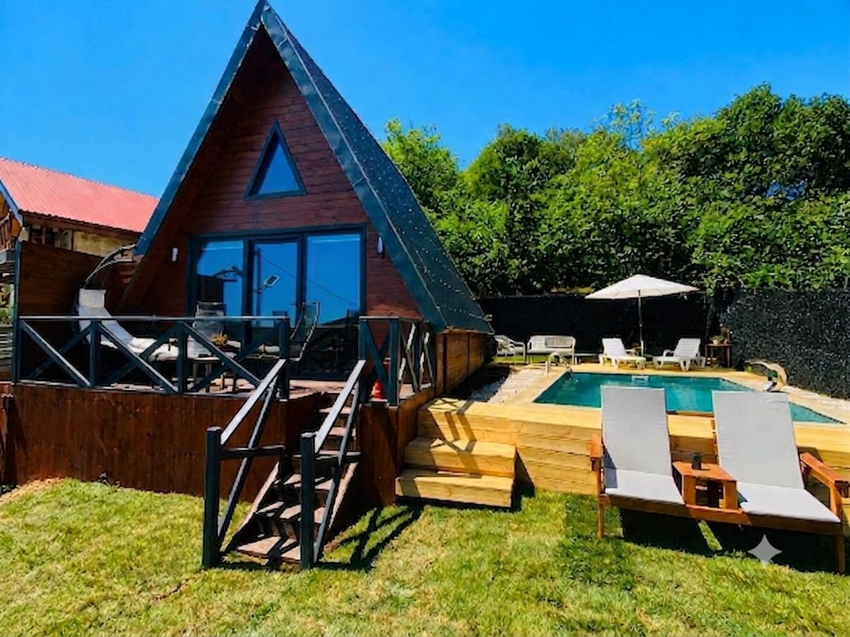 A wooden cabin with a triangular roof, a pool, and outdoor seating.