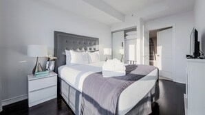 A modern bedroom with a large bed, a nightstand with a lamp, and a wardrobe. - Altitude Suites on Yonge (Toronto)
