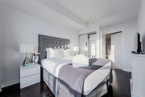 A modern bedroom with a large bed, a nightstand with a lamp, and a wardrobe. - Altitude Suites on Yonge (Toronto)