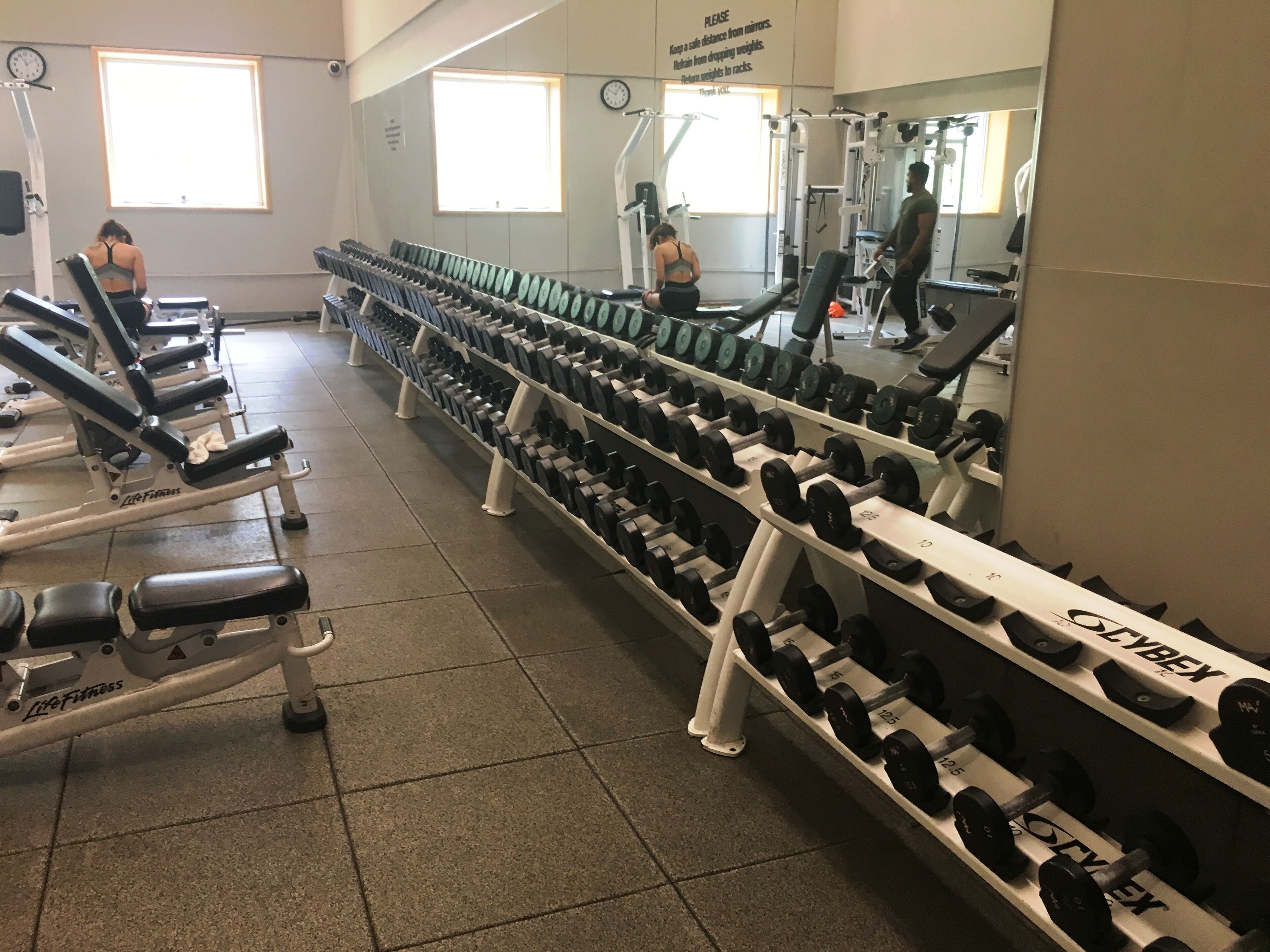 Ein Fitnessraum mit Gewichthebern, darunter Kurzhanteln und Bänke, die in Reihen angeordnet sind.