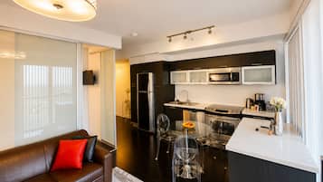 A modern kitchen with stainless steel appliances, a dining area with a glass table, and a living area with a brown leather sofa.
