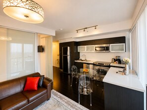 A modern kitchen with stainless steel appliances, a dining area with a glass table, and a living area with a brown leather sofa.