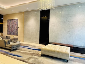 A modern lobby with a plush sofa, a tufted ottoman, a colorful abstract painting, and a large chandelier. - Altitude Suites on Yonge (Toronto)