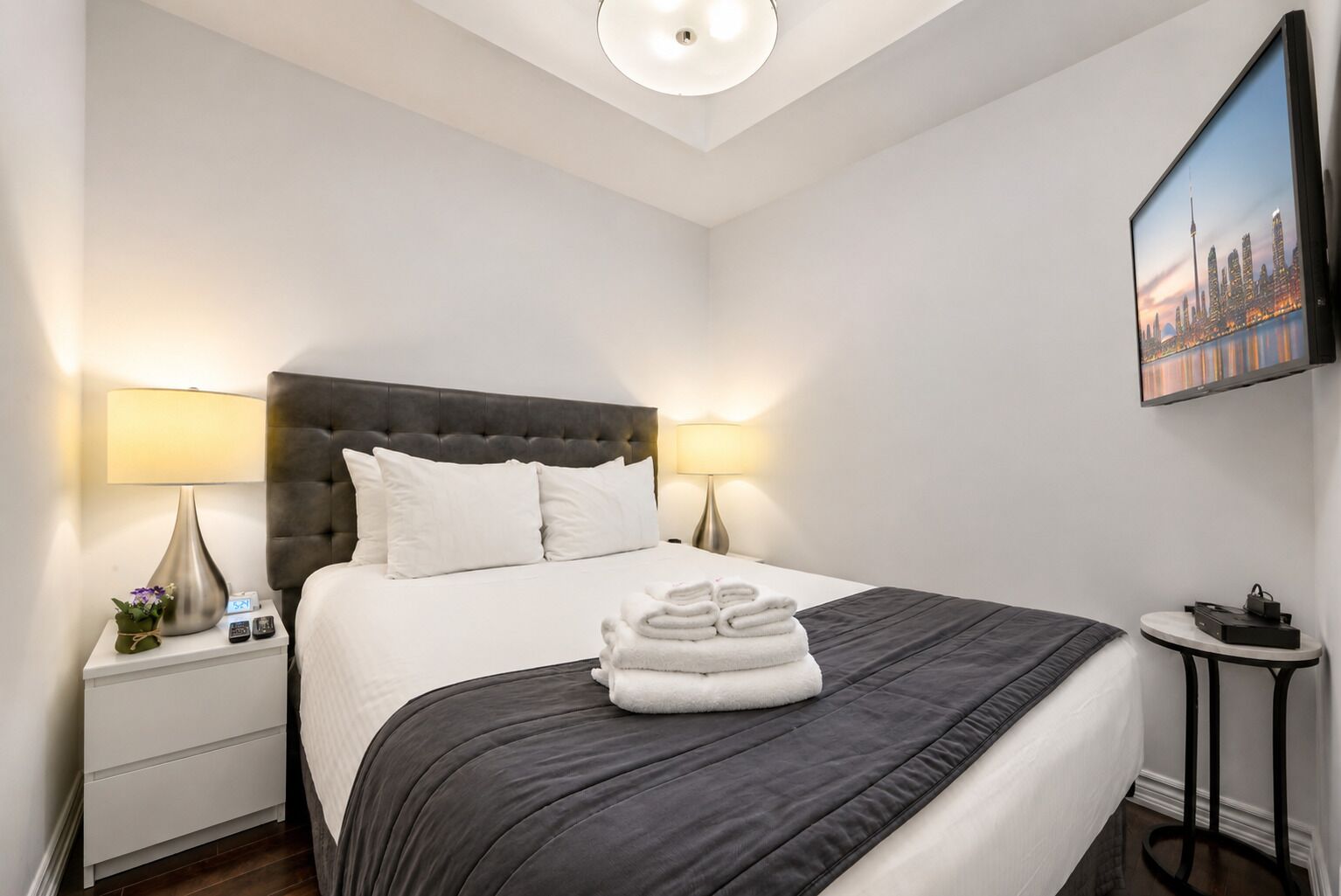 Une chambre d’hôtel avec un grand lit, deux lampes de chevet, une petite table et un téléviseur fixé au mur.