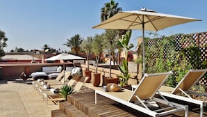 A rooftop lounge area with sun loungers, umbrellas, and potted plants. - Riad Houma (Marrakech)
