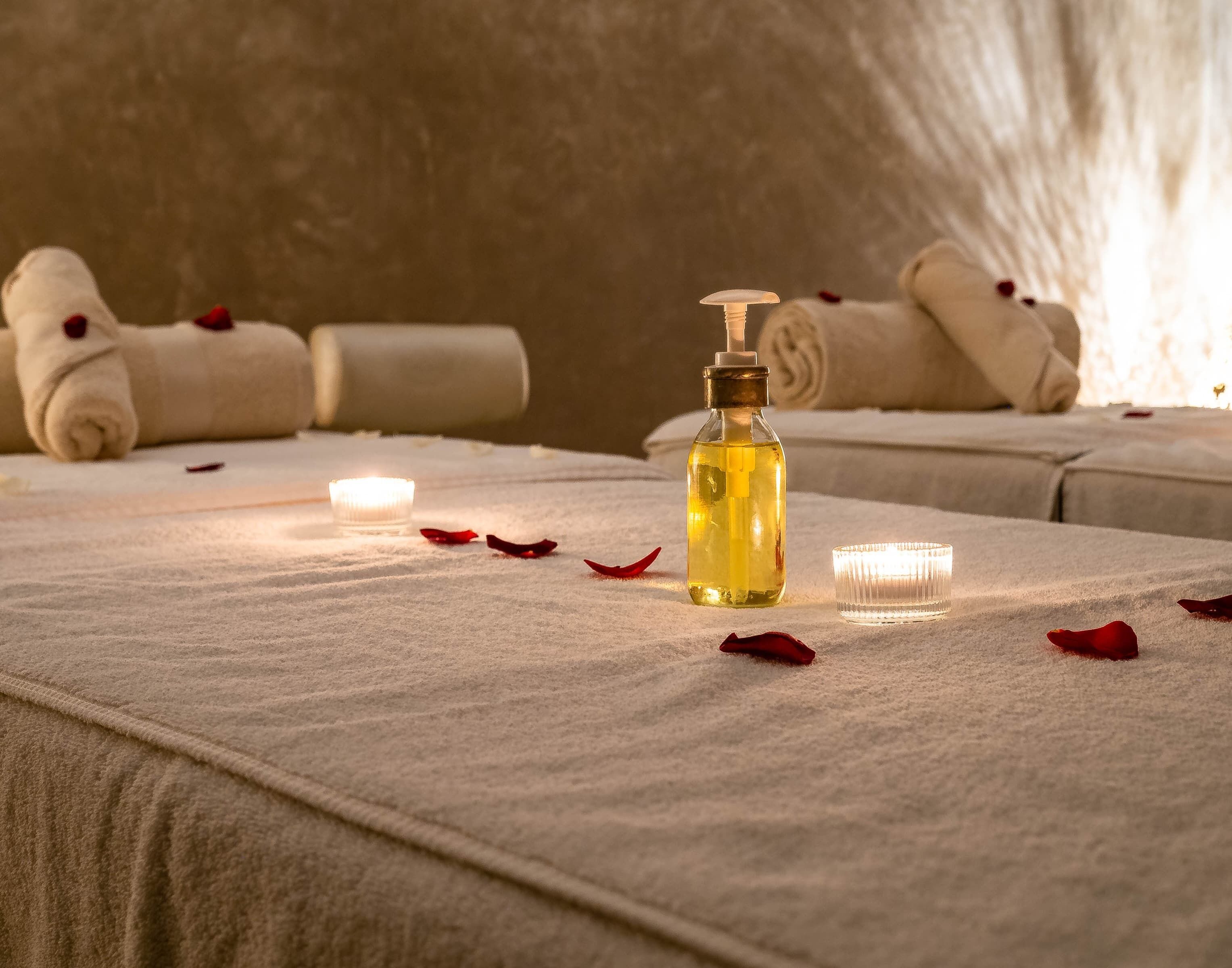 Ein Spa-Raum mit Handtüchern, einer Lotionflasche und Kerzen auf einem Tisch.