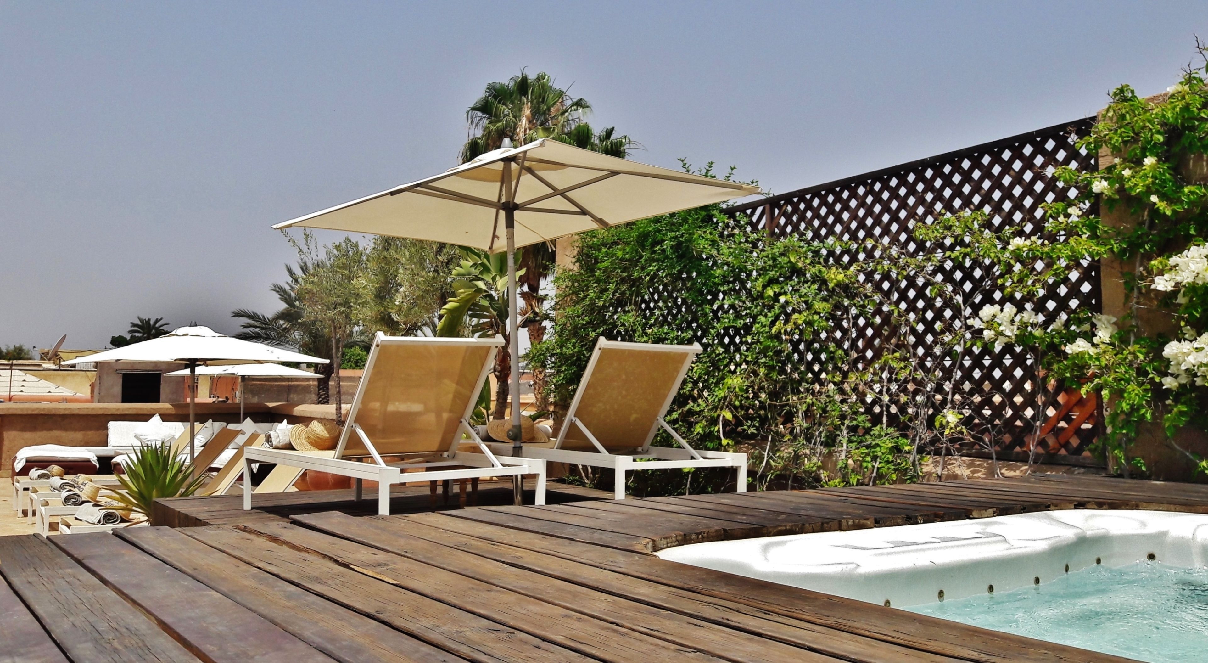 Terraza de madera con dos sillones reclinables y una bañera de hidromasaje blanca.