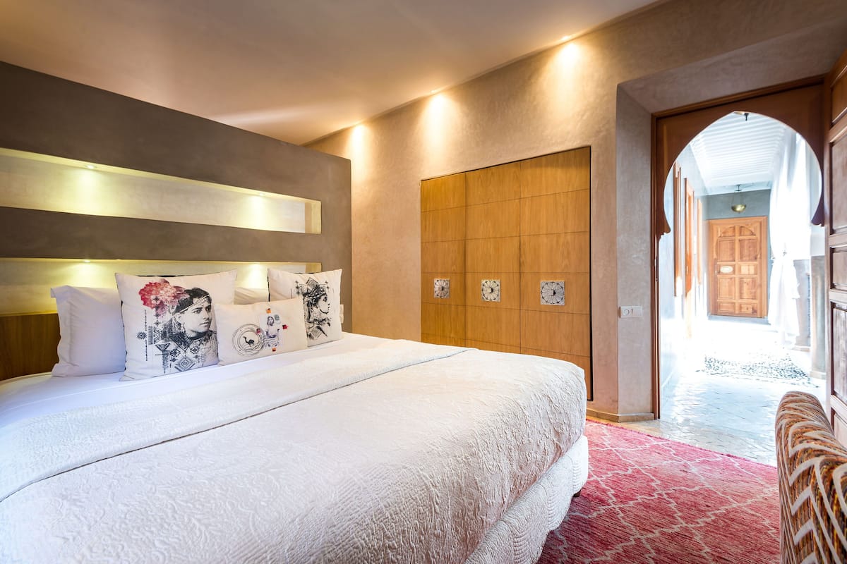 A bedroom with a large bed, a wooden wardrobe, and a red carpet.