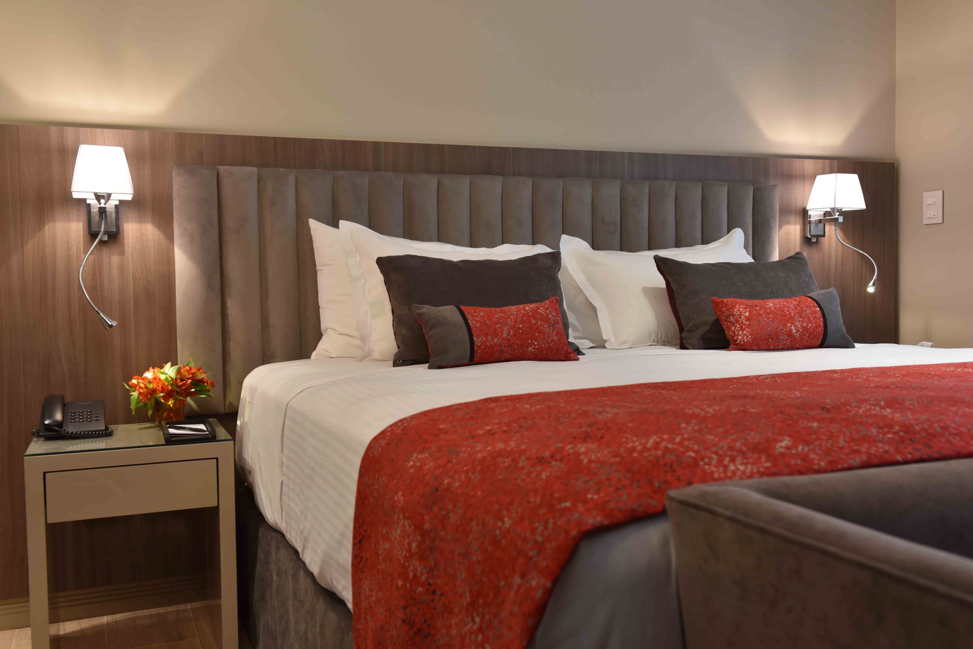 A hotel room with a large bed, two bedside lamps, a nightstand with a phone and a vase of flowers.