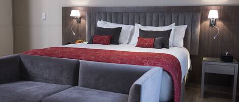 A modern hotel room with a large bed, grey upholstered chairs, a bedside table with a lamp, and a small table with a tissue box.