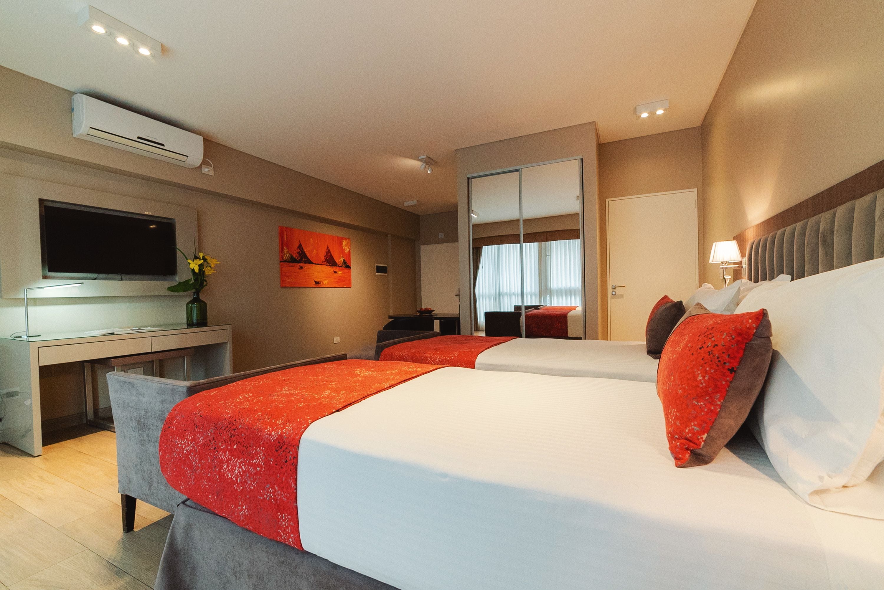 A hotel room with two beds, a desk, a flat-screen TV, and a large mirror.