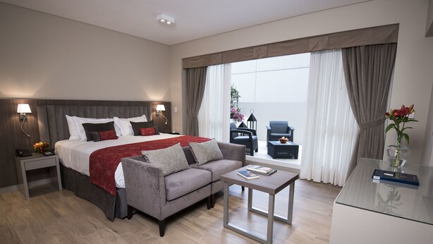 Habitación de hotel moderna con una cama grande, un sofá, una mesita y vistas al exterior.