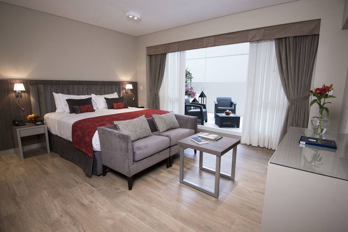 Habitación de hotel moderna con una cama grande, un sofá, una mesita y vistas al exterior.