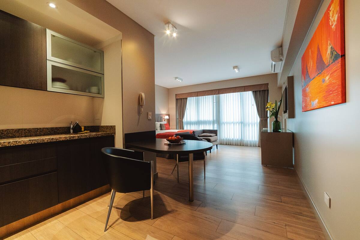 Una cocina moderna con armarios oscuros, encimera de granito y comedor con mesa y sillas negras.