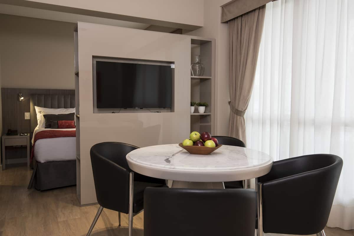 Una habitación de hotel moderna con una cama, un televisor, una mesa de comedor con sillas y un frutero.