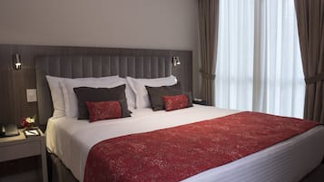 Een hotelkamer met een groot bed, een nachtkastje met een telefoon en lamp, en een raam met gordijnen.