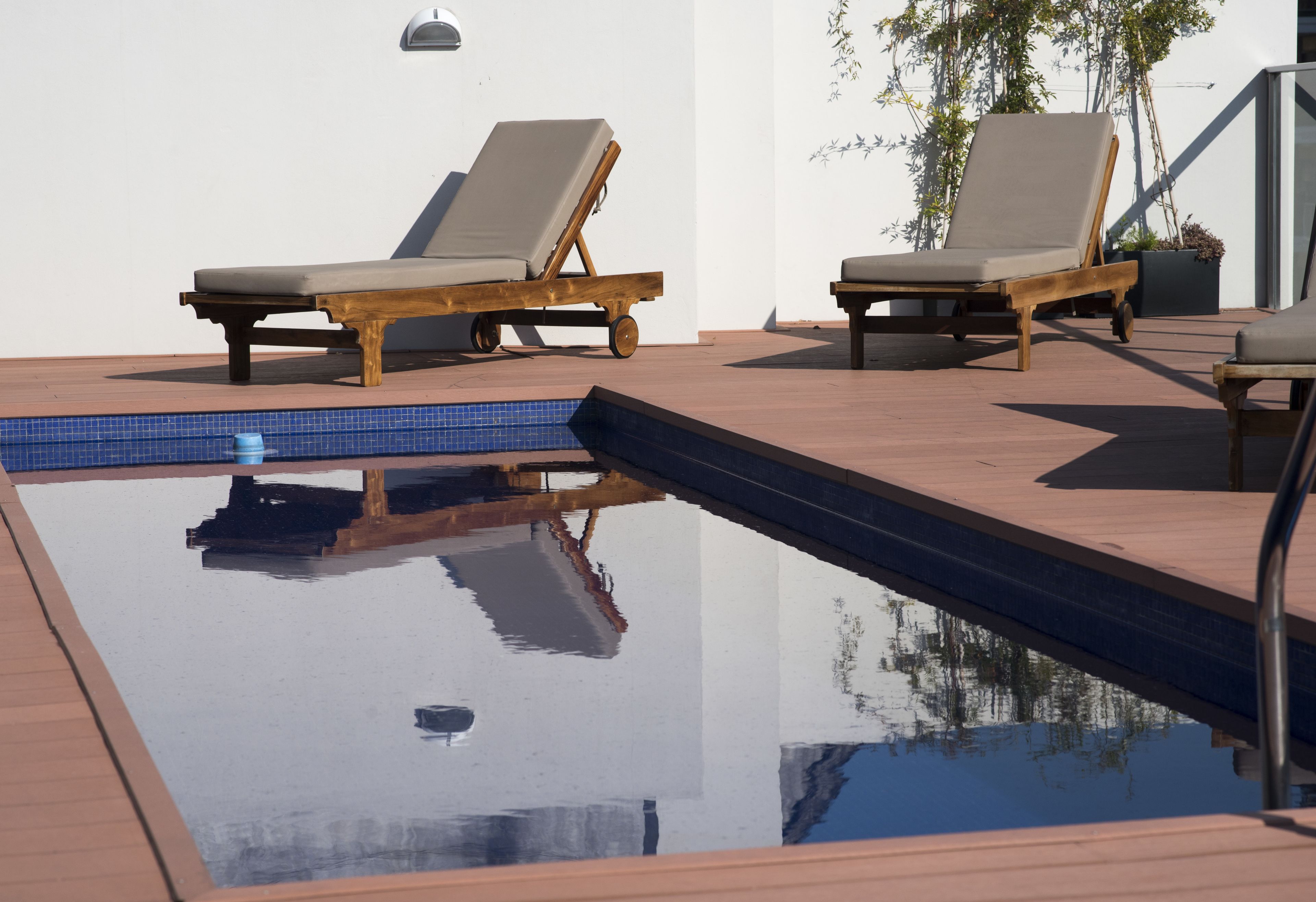 A pool area with two wooden lounge chairs and a potted plant.