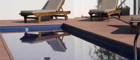 Zona de piscina con dos sillones de madera y una planta en maceta.