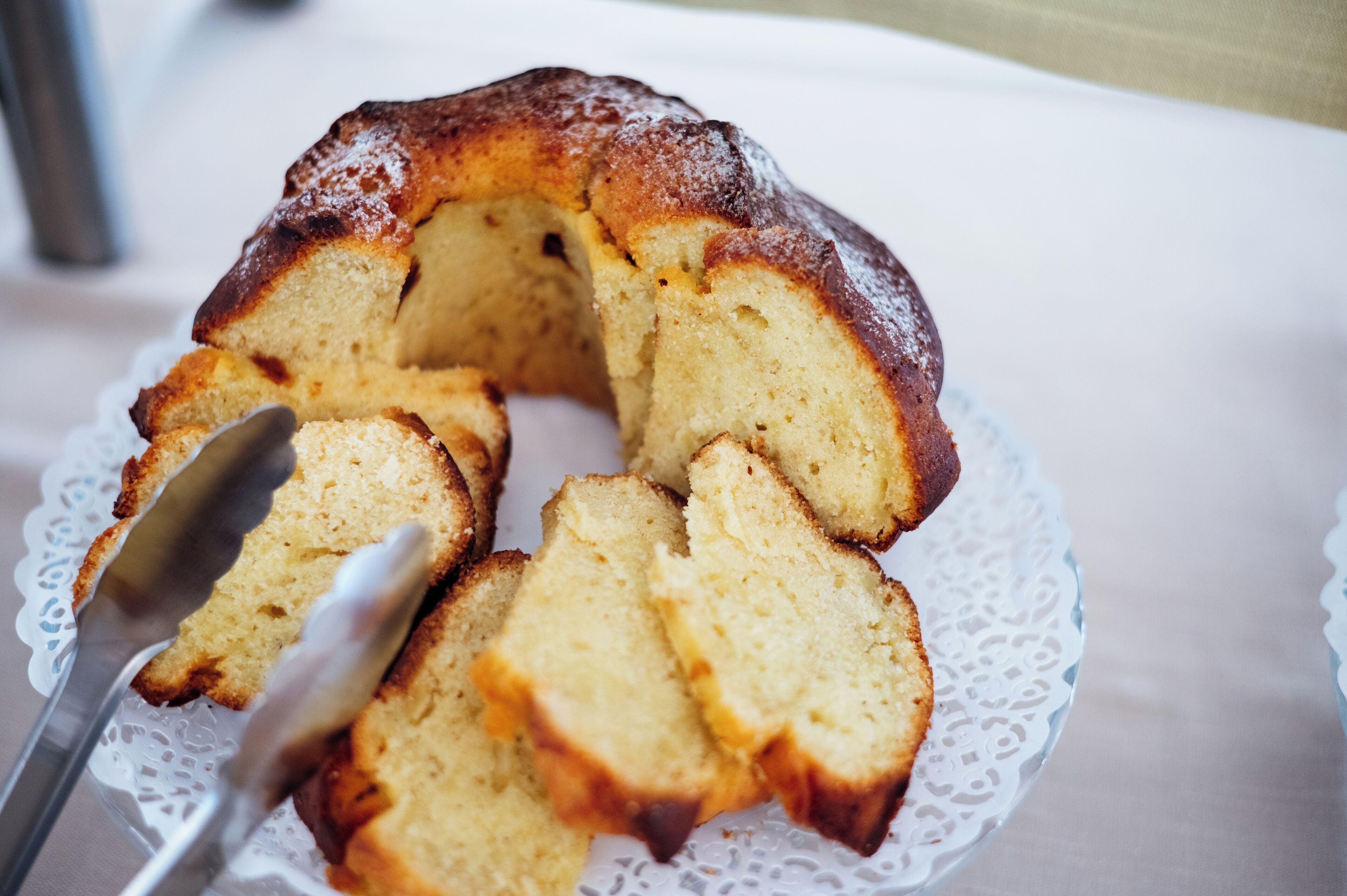 Un pastel bundt en un plato blanco con un mantel de encaje, y una cuchara para cortar una porción.