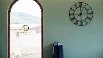 A room with a large clock on the wall, a window with a view of mountains, and a pair of skis leaning against the wall.