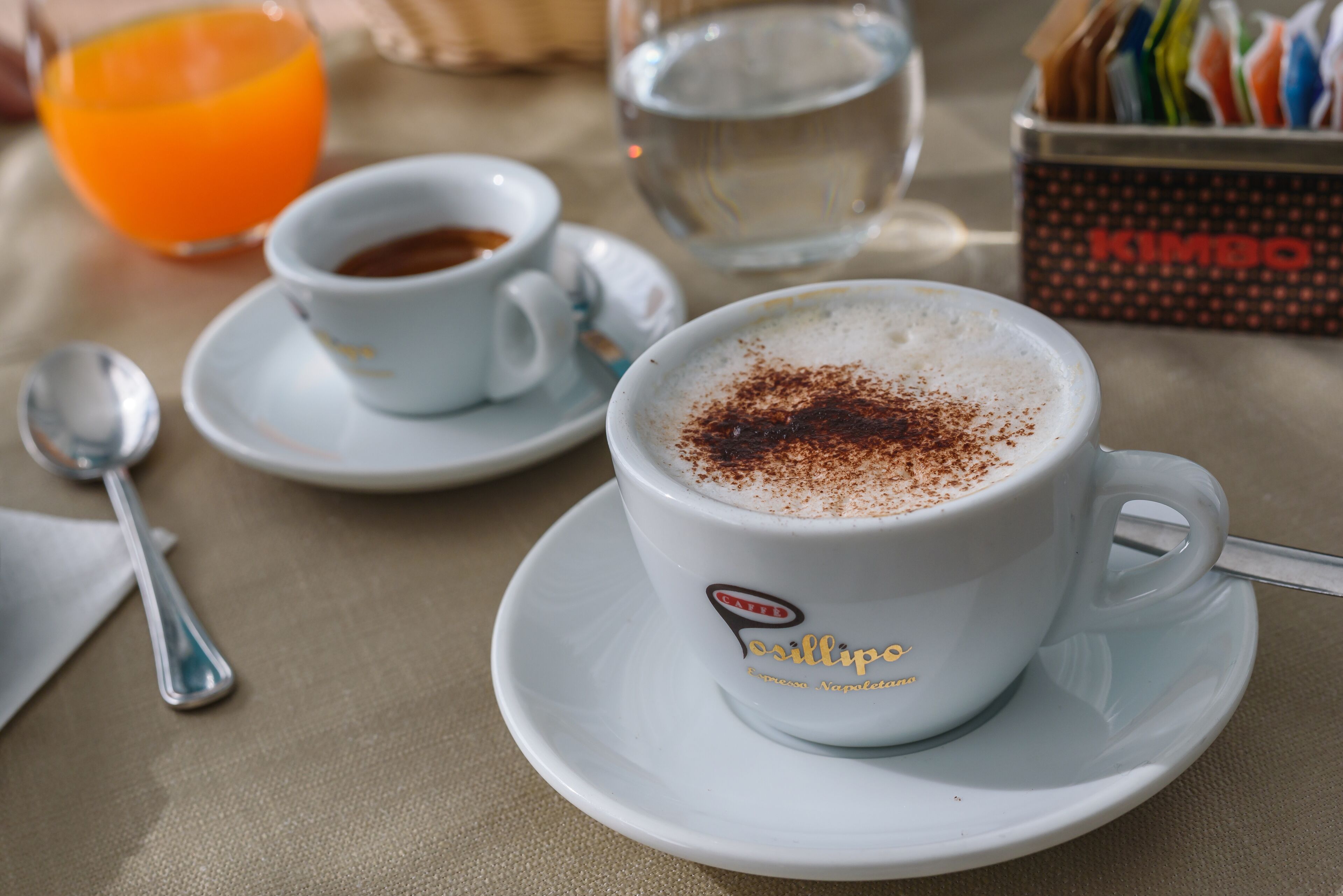 Una mesa con una taza de café, un vaso de jugo de naranja y un vaso de agua.