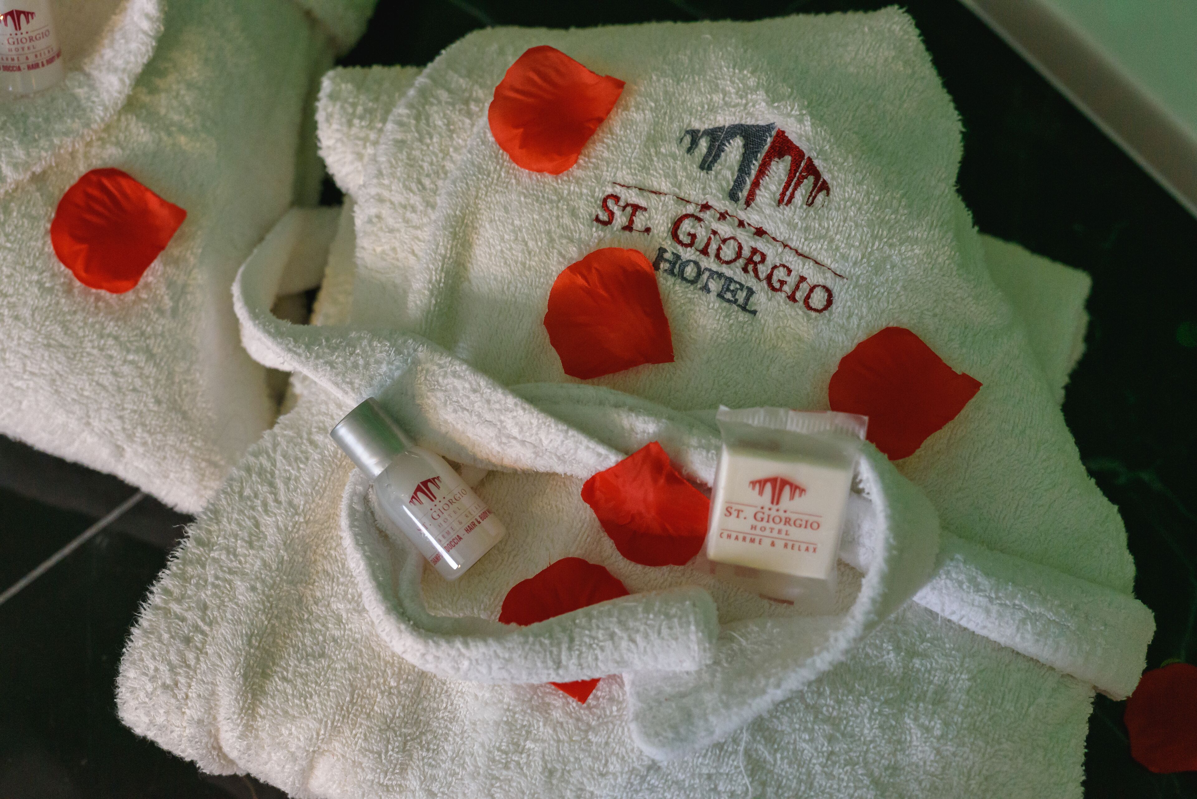 Ein weißes Handtuch mit roten Rosenblättern und dem Logo des Hotels St. Giorgio.