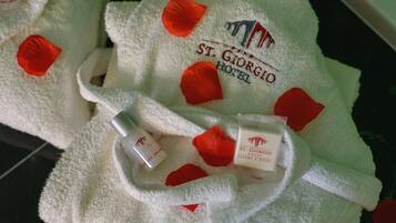 Ein weißes Handtuch mit roten Rosenblättern und dem Logo des Hotels St. Giorgio.