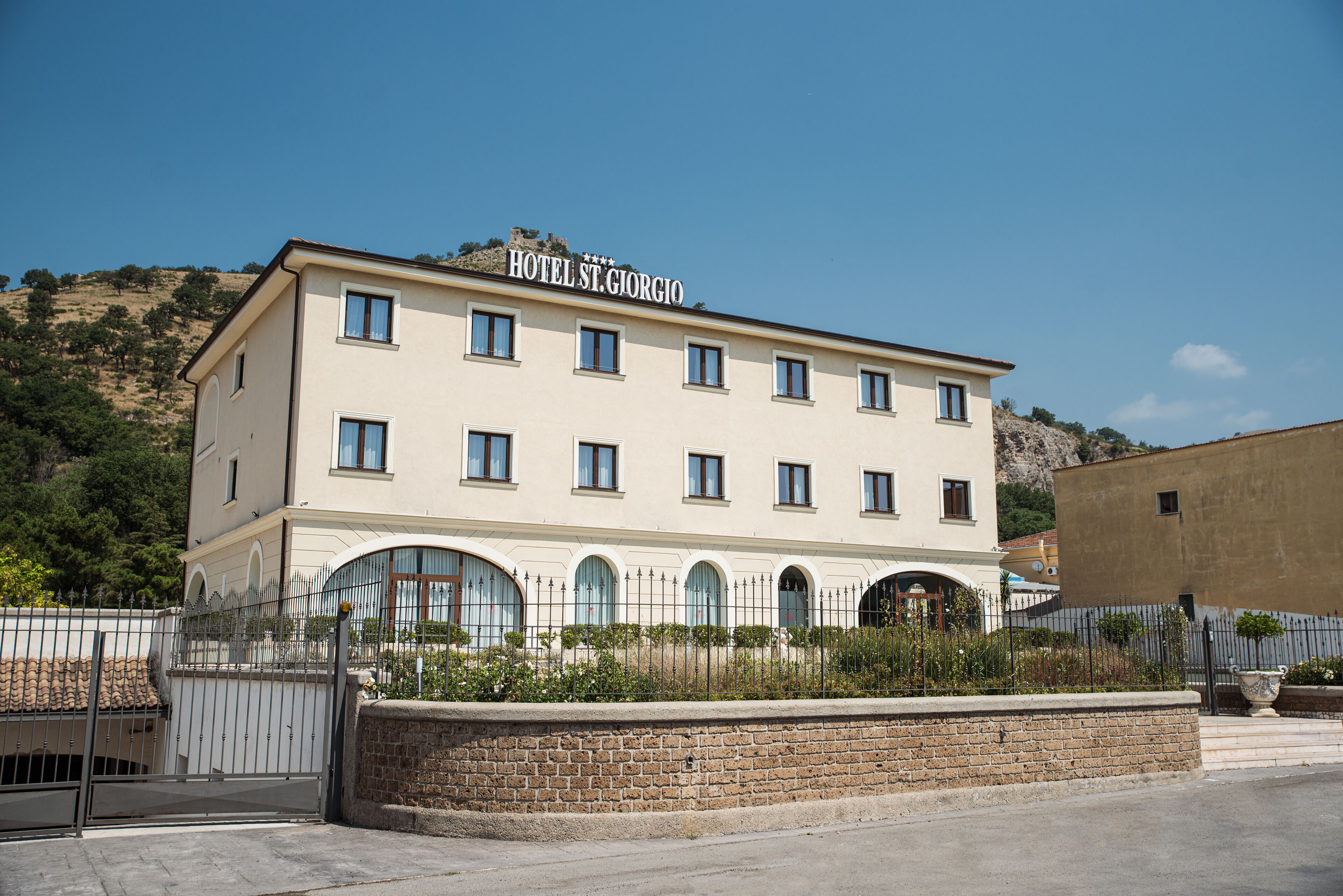 Un hôtel dont l’enseigne indique « HÔTEL ST. GIORGIO », avec une façade symétrique comportant de nombreuses fenêtres et des portes en arc de cercle.