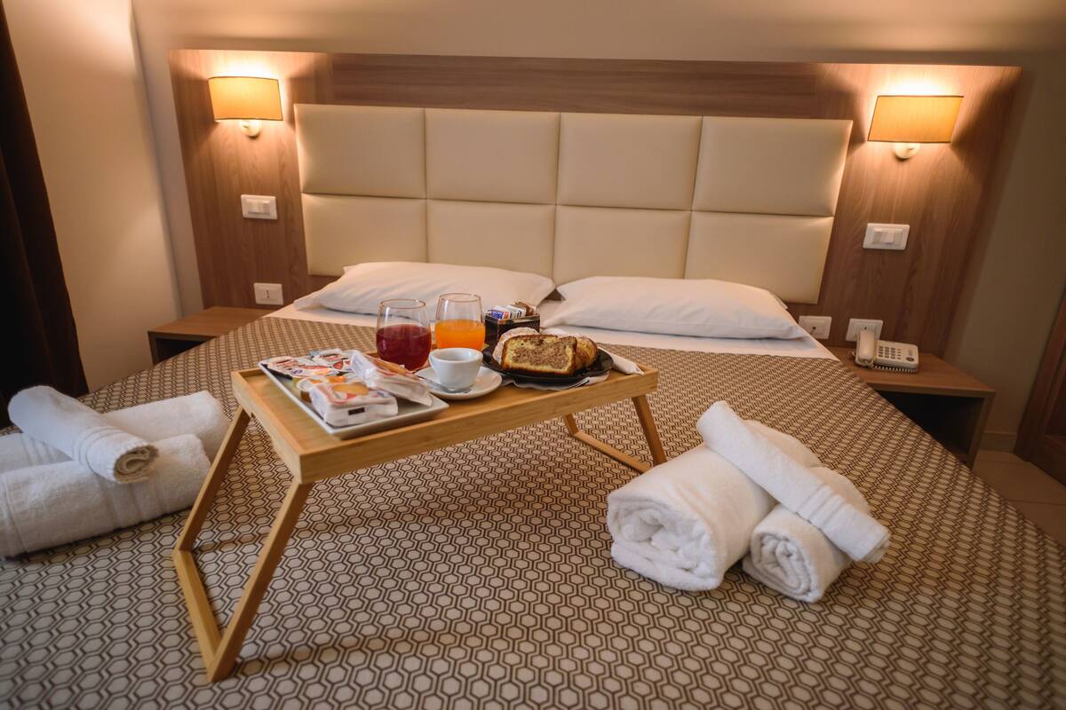 A hotel room with a neatly made bed, a bedside table with breakfast items, and a bedside lamp.