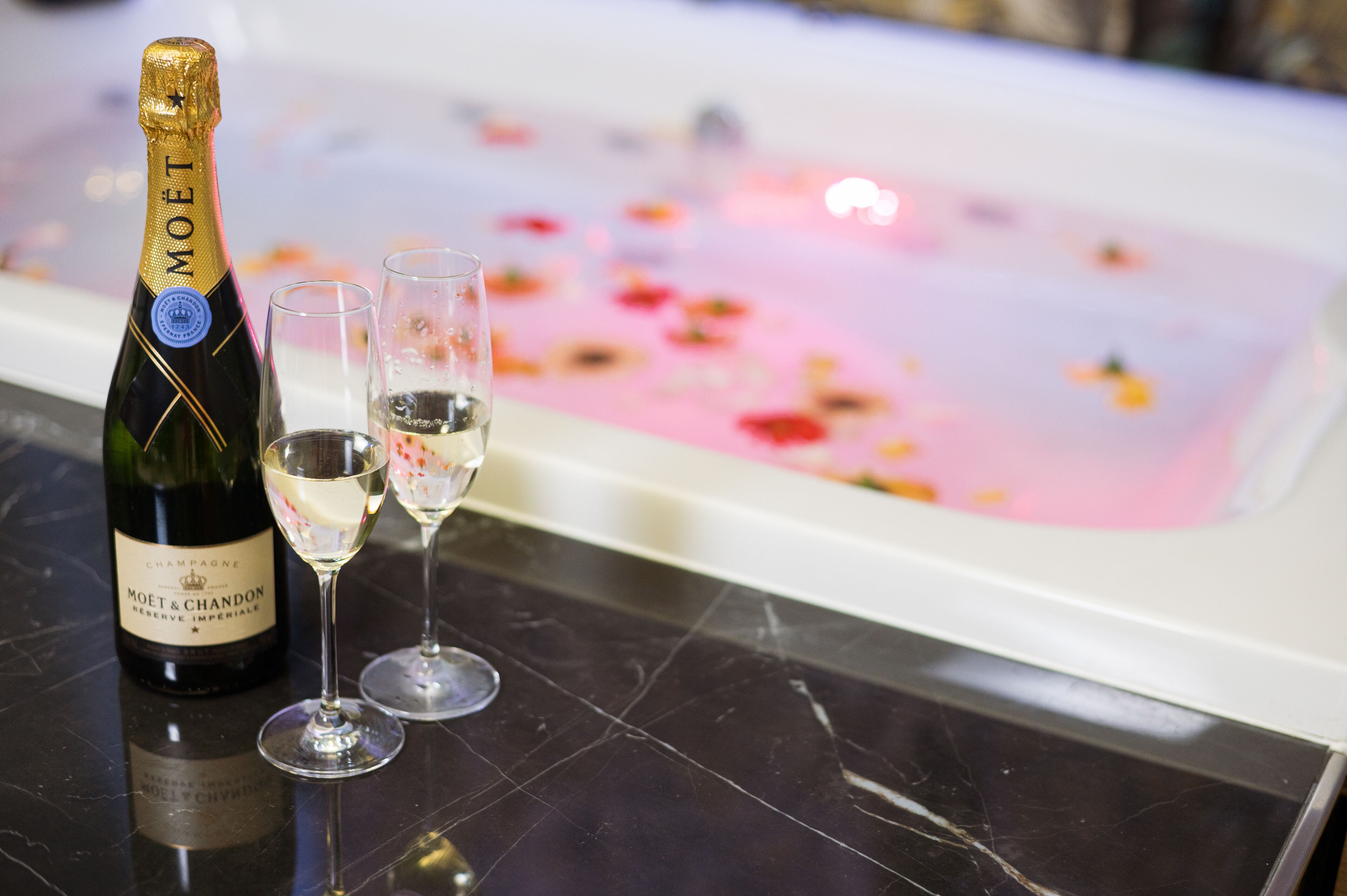 Uma garrafa de champanhe Moët & Chandon e duas taças sobre uma superfície de mármore, com um arranjo floral ao fundo.