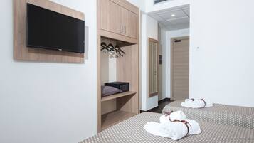 A hotel room with a flat-screen TV mounted on the wall, a wooden wardrobe, a bed with patterned bedding, and two rolled towels on the floor.