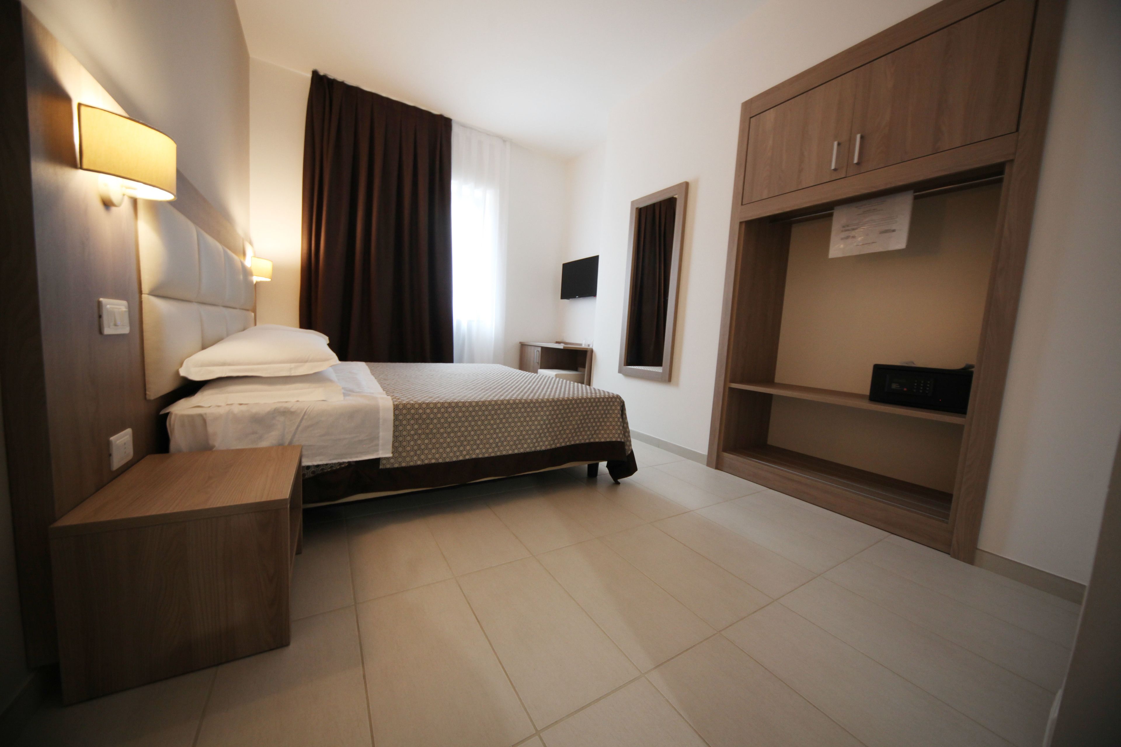 Una camera d'albergo con un letto, un comodino, un armadio e una televisione.