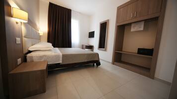Una camera d'albergo con un letto, un comodino, un armadio e una televisione.