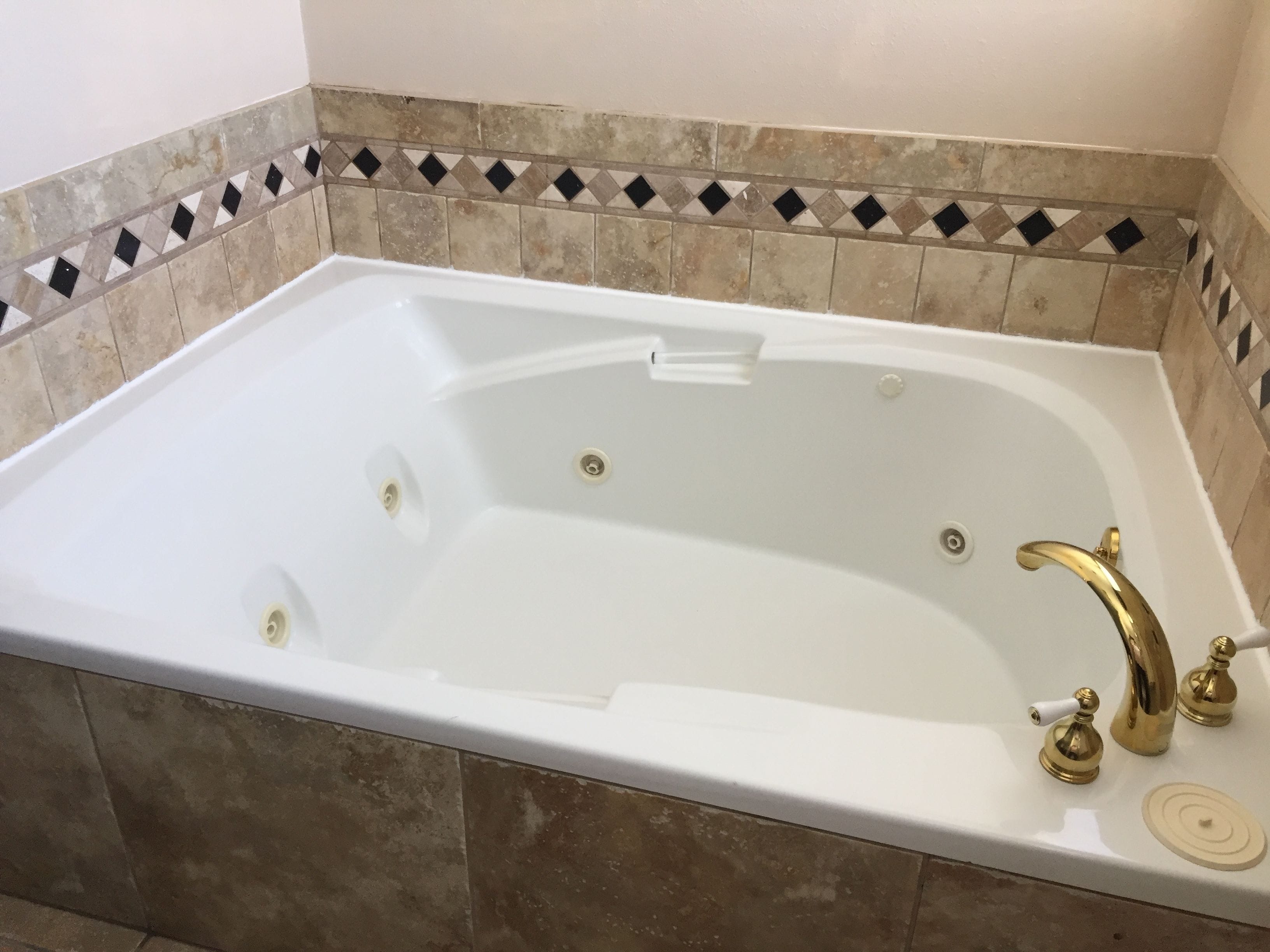 Una vasca da bagno rettangolare con interni bianchi, rubinetteria dorata e rivestimento piastrellato.