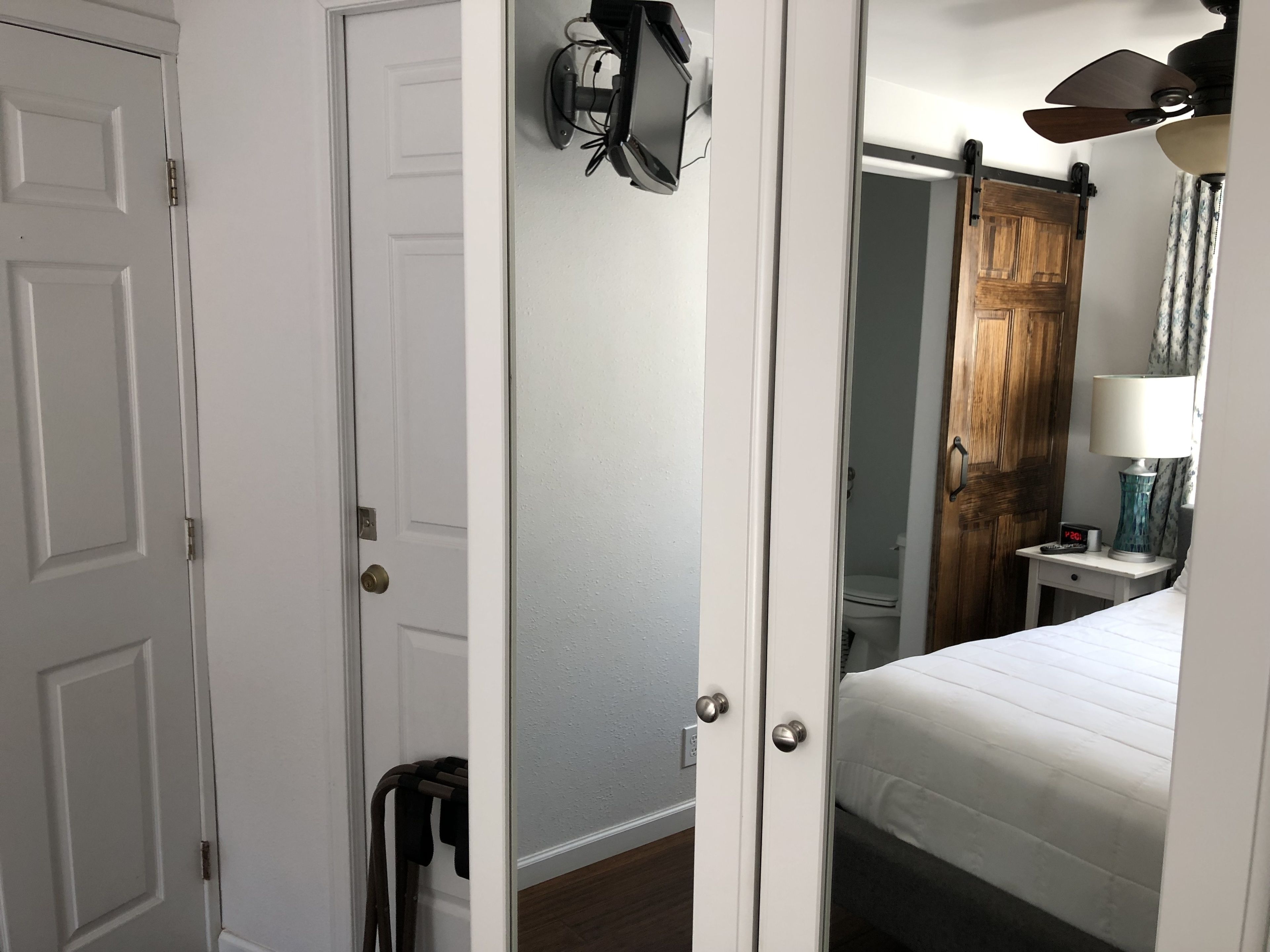 A bedroom with a bed, a nightstand, a lamp, a wooden door, and a white wall.