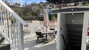 A balcony with a table and chairs, a white railing, and a view of a hillside with buildings.