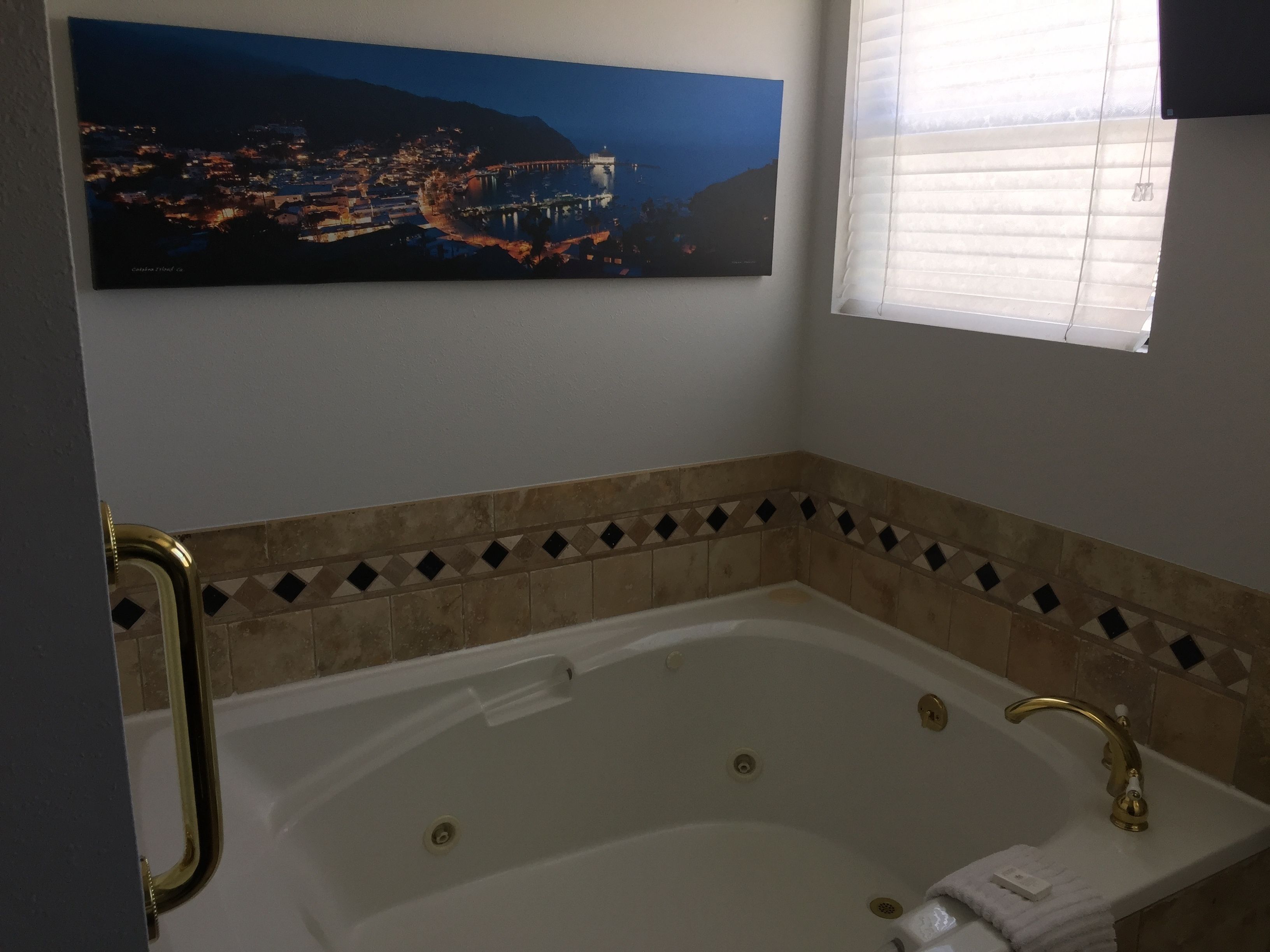 A bathroom with a large bathtub, a gold faucet, and a tiled border.