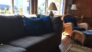 A room with a dark grey sofa, a wicker chair, and a small table with a lamp.