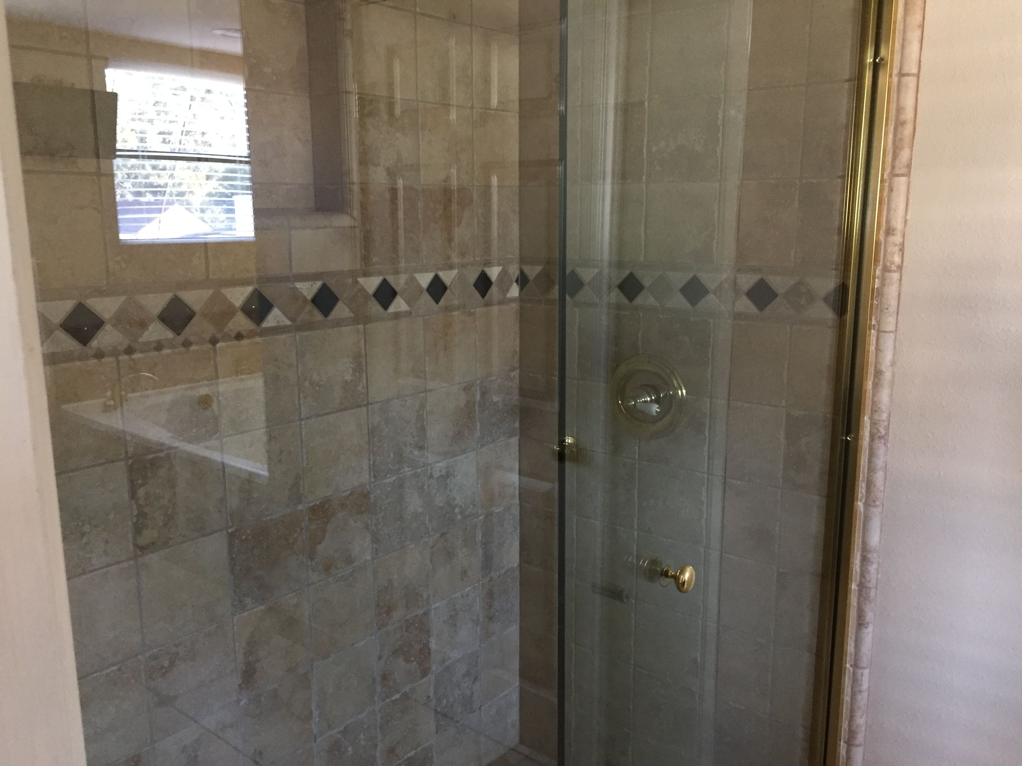 A glass-enclosed shower with a tiled wall, a small window, and a door with a brass handle.