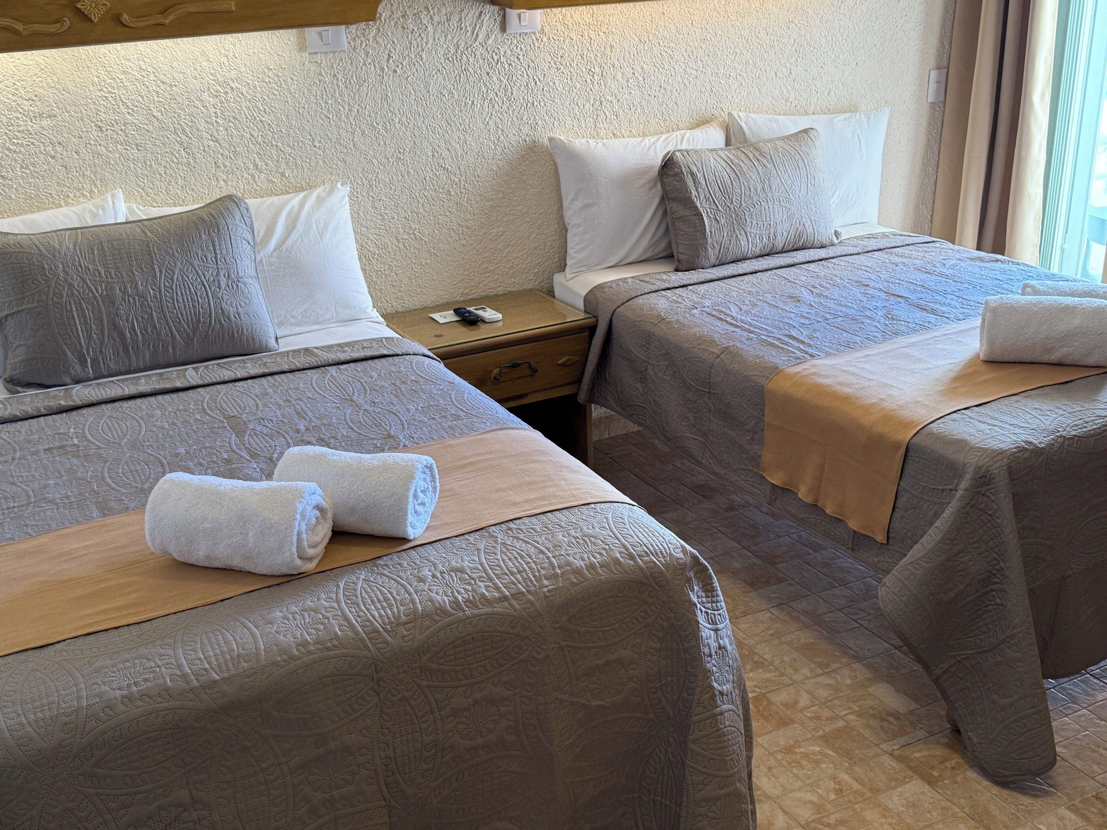Une chambre d’hôtel avec deux lits, chacun doté d’une tête de lit en bois, d’une table de chevet et d’un petit tiroir.