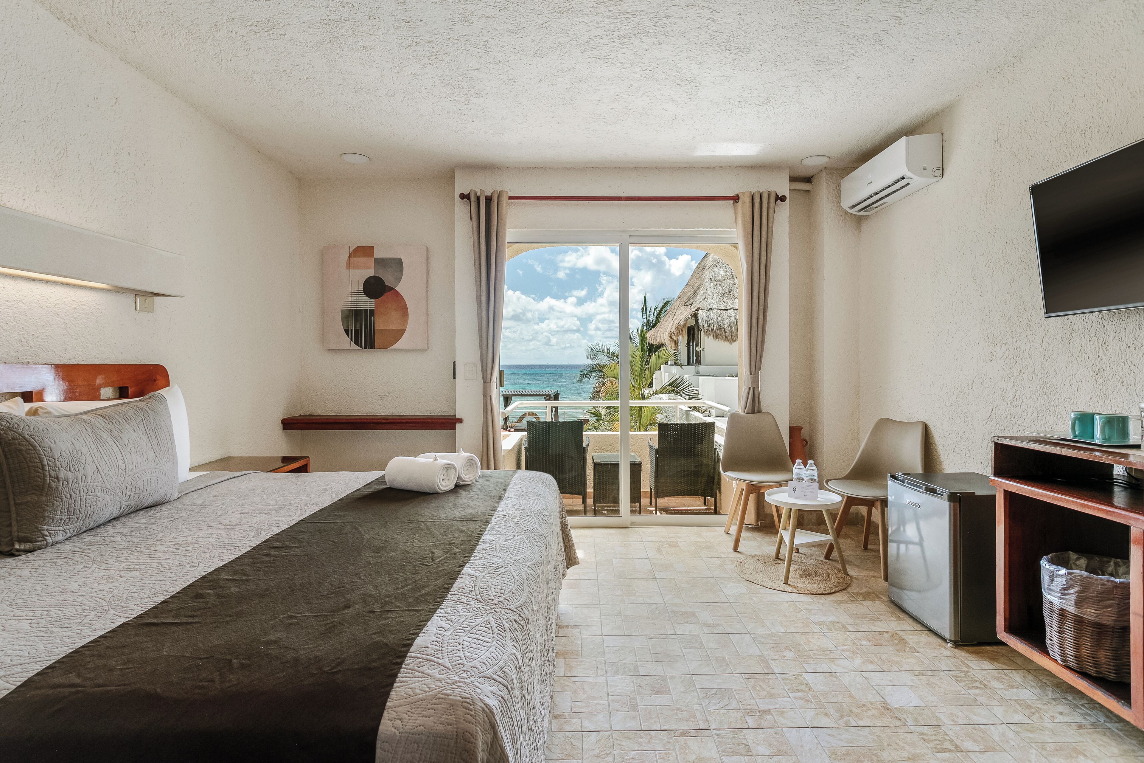 A hotel room with a bed, a desk, a chair, a TV, and a view of the ocean.