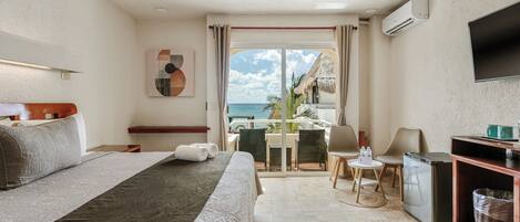 A hotel room with a bed, a desk, a chair, a TV, and a view of the ocean.