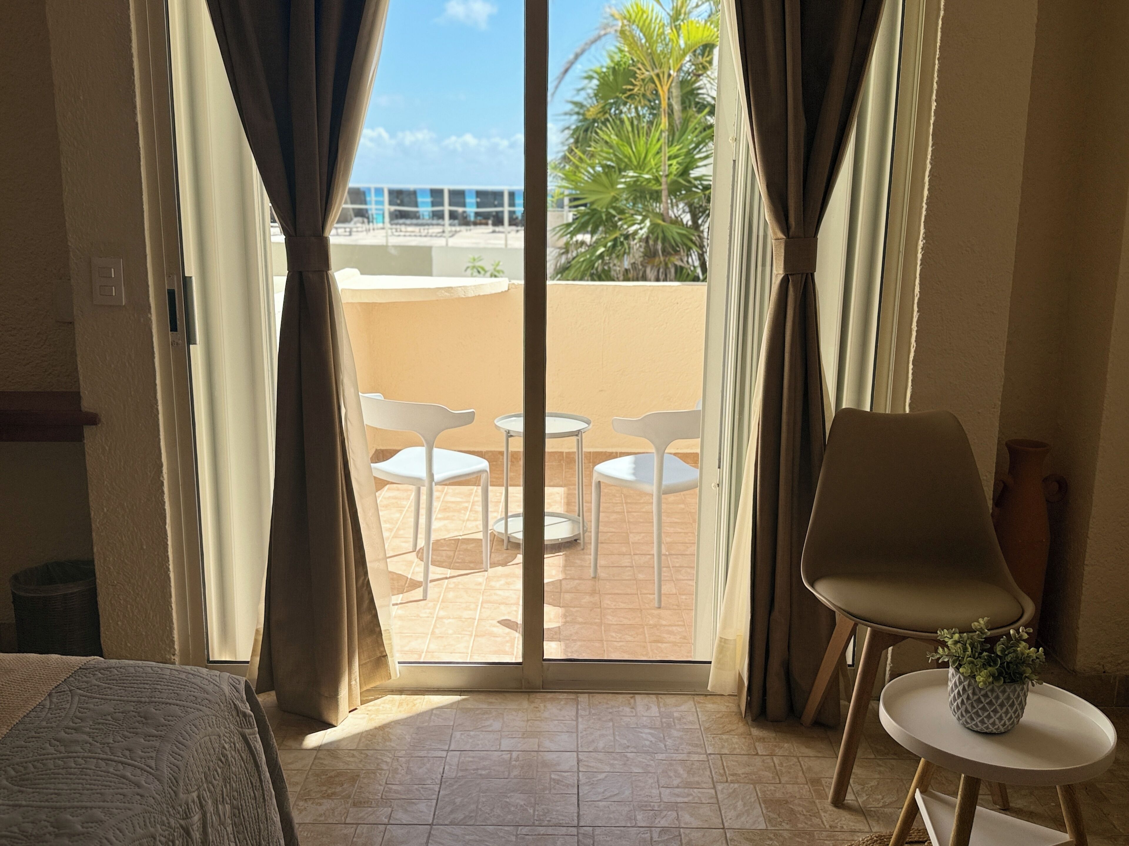 A room with a sliding glass door leading to an outdoor patio with white chairs and a table.