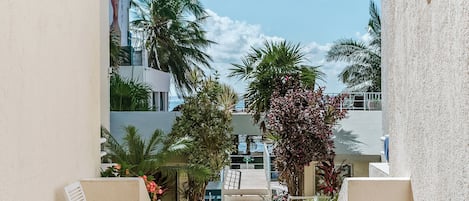 A courtyard with white chairs, potted plants, and a view of palm trees and buildings.