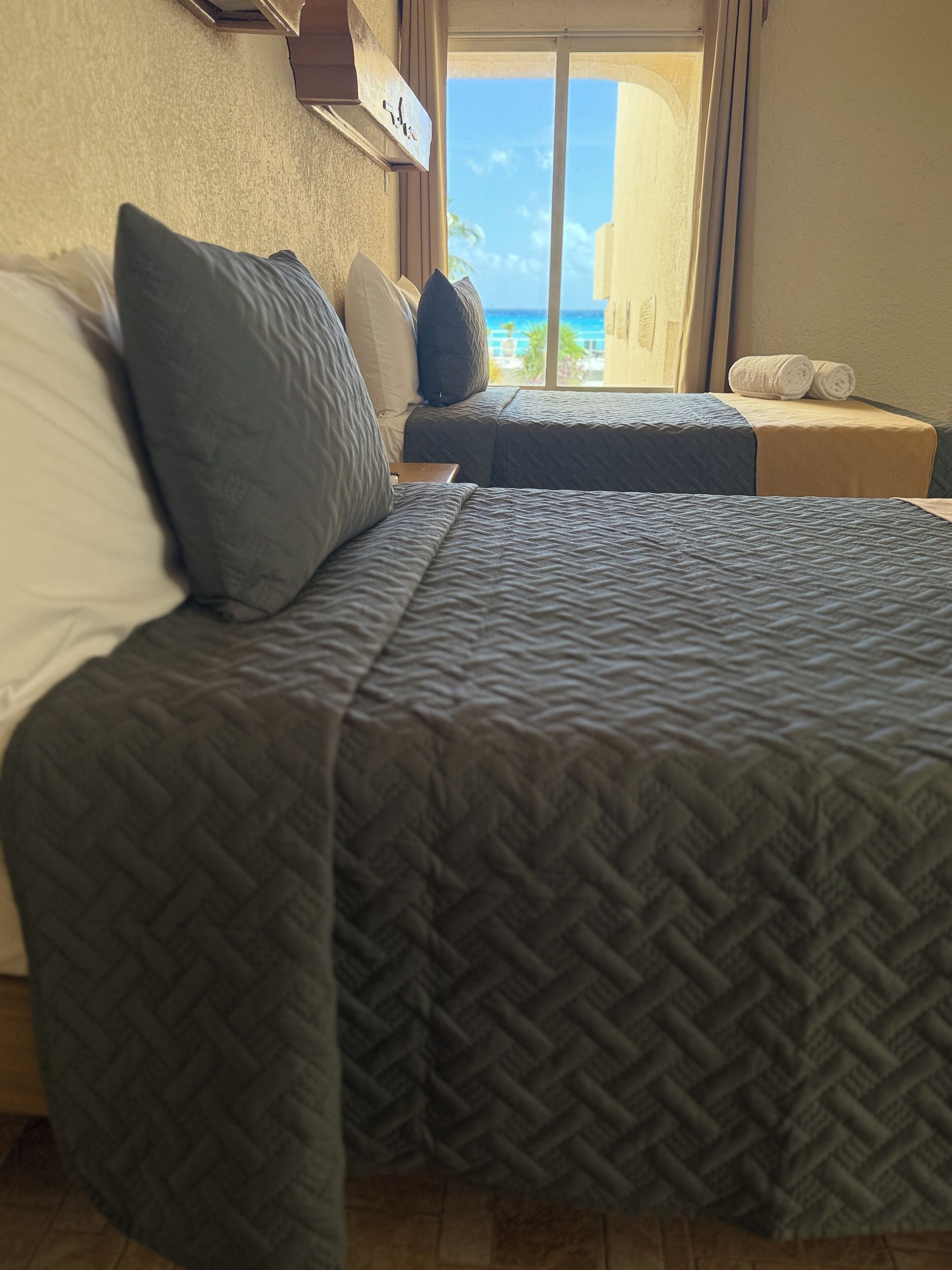 A hotel room with two beds, a view of the ocean, and a small table with towels.