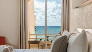 Una habitación de hotel con cama, vistas al océano y un balcón con mesa y sillas.